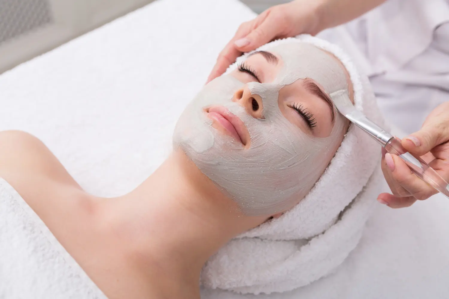 Face peeling mask, spa beauty treatment, skincare. Woman getting facial care by beautician at spa salon, side view, close-up