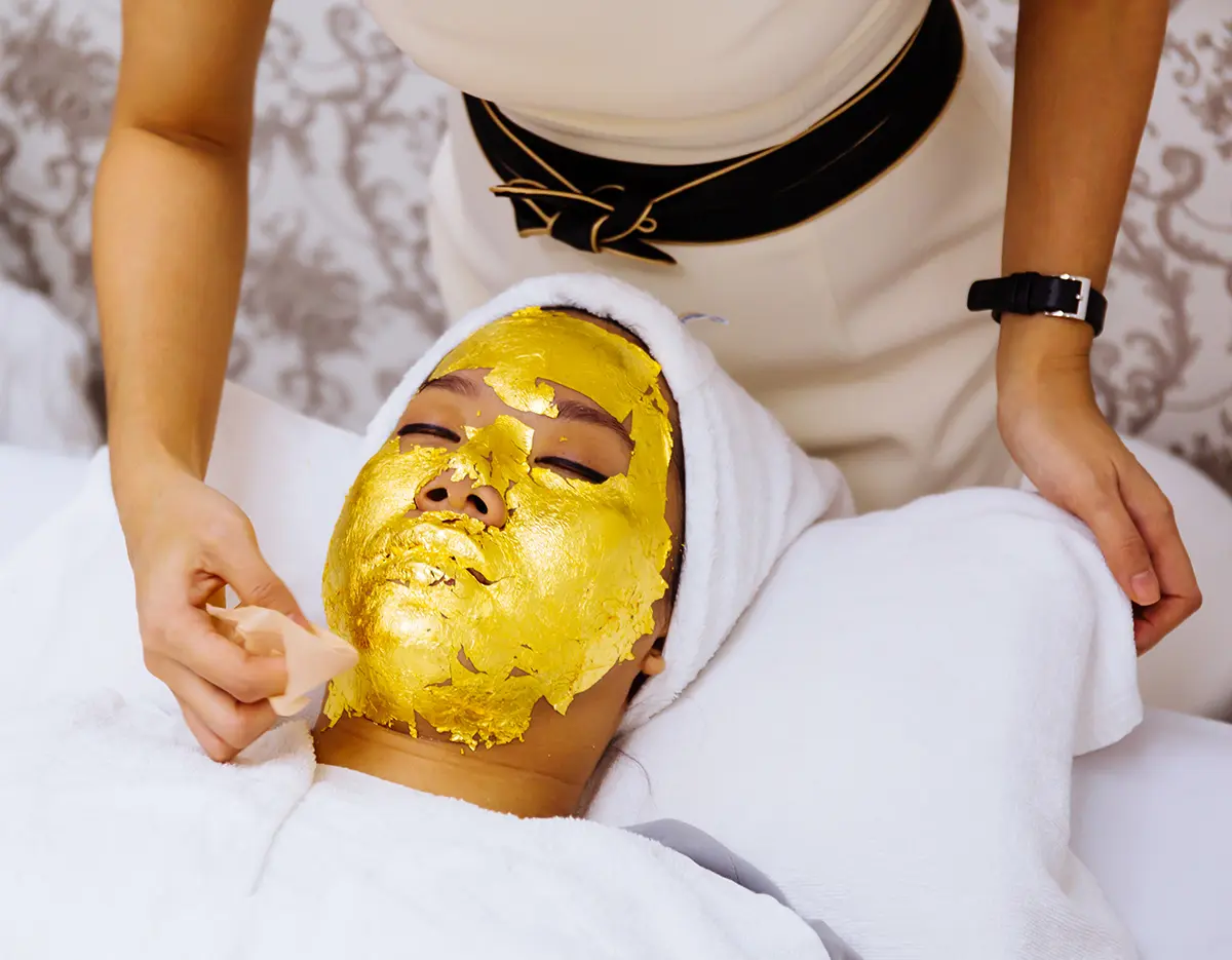Beauty clinic staff helping young woman getting 24 karat gold facial treatment at the beauty clinic. The treatment of using real gold for youthful skin